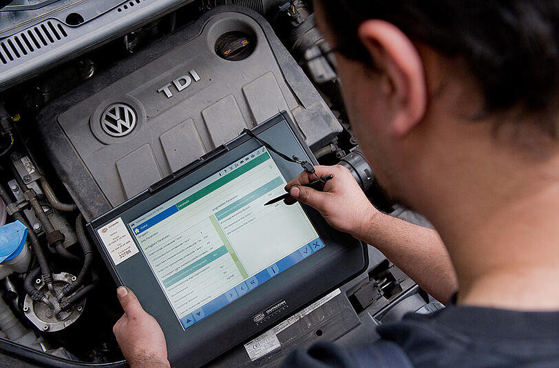 Ein KFZ-Servicetechniker steht mit einem Auslesegerät vor einem vom Abgas-Skandal betroffenen 2.0l TDI Dieselmotor vom Typ EA189 in einem VW Touran.