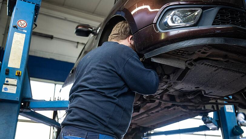 Ein Mechaniker schaut in einer Kfz-Werkstatt in den Radkasten eines Autos.