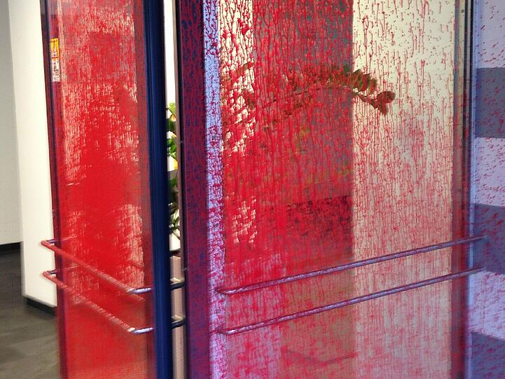 Die gesamte Eingangstür ist voll roter Farbe. Will man die Tür aufmachen, kommt man nicht umhin, in rote Farbe zu fassen.