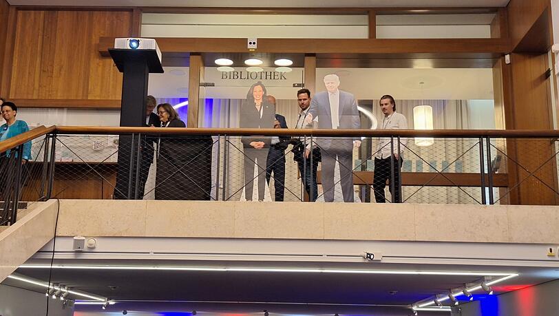 Trump und Harris lächeln auf die Gäste im Foyer des Amerikahauses in München hinab. Trump und Harris lächeln auf die Gäste im Foyer des Amerikahauses in München hinab.
