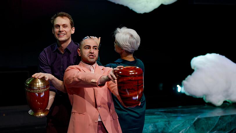 Yascha Finn Nolting (l-r), Aydin Aydin und Adeline Schebesch preisen verschiedene Urnen an in dieser Szene des Theaterstücks "Exit - Sterben für Anfänger*innen" im Staatstheater Nürnberg.