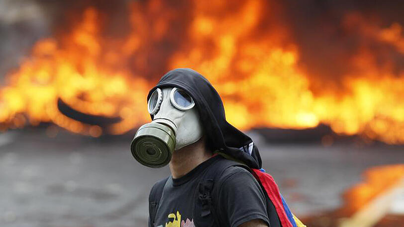 Ein Demonstrant mit einer Gasmaske steht in Caracas während eines Protests gegen den sozialistischen Präsidenten Maduro vor einer brennenden Barrikade auf einer Autobahn.