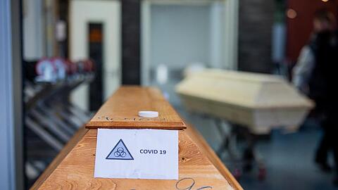 Ein Sarg mit der Aufschrift "Covid 19" und dem Zeichen "Biohazard" steht in einem Krematorium.