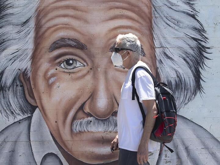 Ein israelischer Mann, der einen Mund- und Nasenschutz trägt, geht an einem Wandbild vorbei, das Albert Einstein zeigt.
