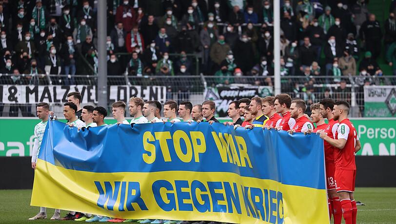 Die Spieler halten zu Spielbeginn eine ukrainische Flagge mit der Aufschrift "Stop War. Wir gegen Krieg.".