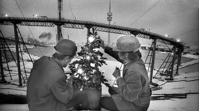 Dezember 1970: Bauarbeiter entzünden einen kleinen Christbaum auf der Haupttribüne des Olympiastadions, das noch eine Großbaustelle ist.