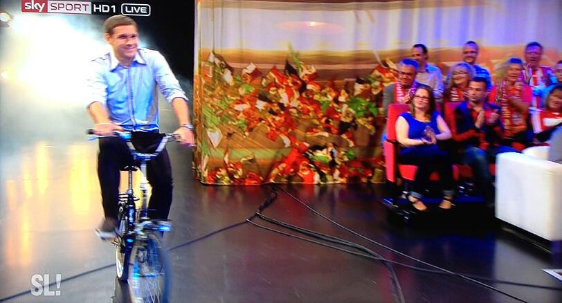 Mit dem Klapprad kommt Löwen-Profi Moritz Volz nicht nur in die Sky-Sendung "Samstag Live" eingefahren...