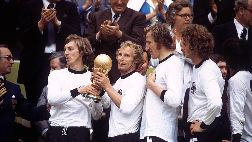 Die BR Deutschland ist Weltmeister 1974 - Jürgen Grabowski (li.) und Berti Vogts präsentieren stolz den Weltpokal, daneben u.a. Rainer Bonhof (2.v.re.) und Hans Georg Schwarzenbeck (3.v.re.). Die BR Deutschland ist Weltmeister 1974 - Jürgen Grabowski (li.) und Berti Vogts präsentieren stolz den Weltpokal, daneben u.a. Rainer Bonhof (2.v.re.) und Hans Georg Schwarzenbeck (3.v.re.).