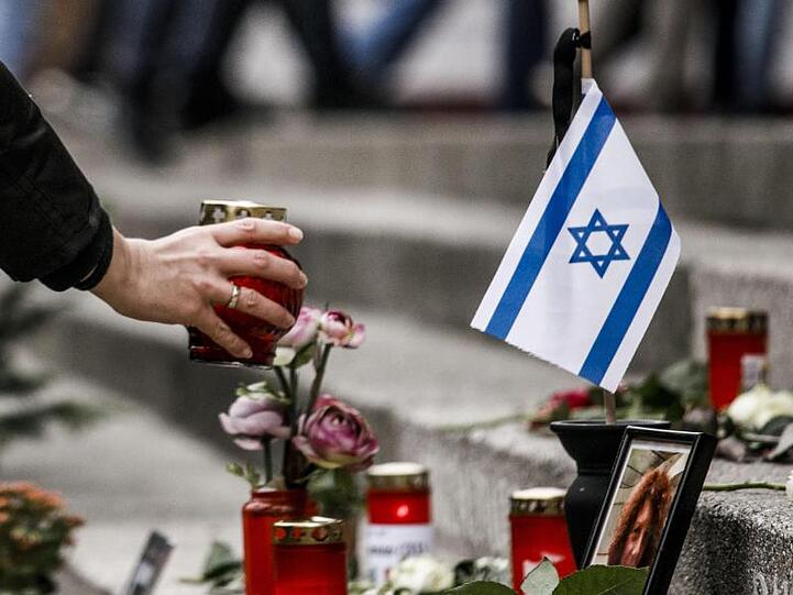 Eine Frau zündet am Breitscheidplatz am Mahnmal vor einer israelischen Fahne ein Kerzenlicht ab.