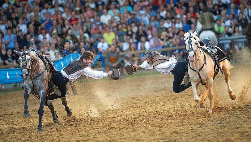 Zwei Stuntmen prosten sich mit Bierkrügen zu, während sie nebeneinander herreiten. Derlei Stunts sind fester Bestandteil des Kaltenberger Ritterturniers. Zwei Stuntmen prosten sich mit Bierkrügen zu, während sie nebeneinander herreiten. Derlei Stunts sind fester Bestandteil des Kaltenberger Ritterturniers.