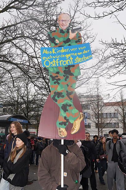 Merz als Karikatur: Provokantes Plakat bei der Demo.