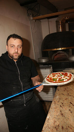 Pizzabäcker Alessandro schiebt die Teigscheibe in den extra aus Italien angelieferten Ofen. In nur 90 Sekunden ist sie dann fertig.
