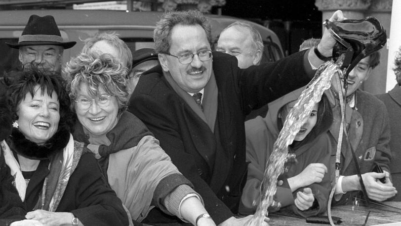 Zum ersten Mal mit "Hacker-Pschorr"-Brunnenrandwerbung: Münchens Oberbürgermeister Christian Ude (r) wäscht am Mittwoch (17.02.1999) in Anwesenheit von Bürgermeisterin Gertraud Burkert (M) und Stadträtin Barbara Seuble-Schaefer (l) im Fischbrunnen am Münchner Marienplatz den Geldbeutel der Stadt. (Archiv)