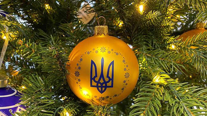 An einem geschmückten Baum hängt eine Kugel in den ukrainischen Nationalfarben und dem Dreizack als Wappen.