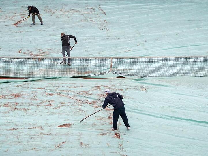 Helfer schieben auf dem Center-Court während einer Unterbrechung wegen Regens das Wasser von einer Abdeckplane. Foto: Daniel Karmann