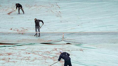 Helfer schieben auf dem Center-Court während einer Unterbrechung wegen Regens das Wasser von einer Abdeckplane. Foto: Daniel Karmann