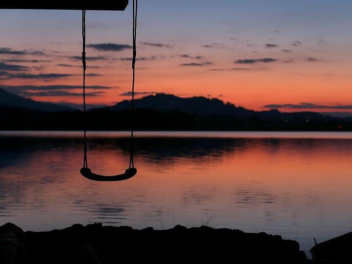 Eine Kinderschaukel hängt an einem Bootshaus am Ufer des Hopfensees im Sonnenuntergang. Foto: Karl-Josef Hildenbrand/Archiv