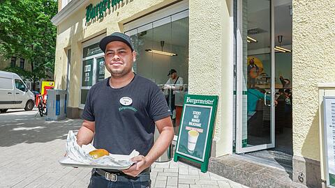Mitarbeiter Adnan (30) hält vor der neuen Burgermeister-Filiale in der Feilitzschstraße einen „Fleischmeister“ (8.99 Euro) in der Hand. Das Lokal ist kurz nach seiner Eröffnung gut besucht.