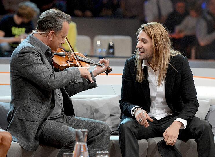 Schaupieler Tom Hanks darf anschließend auch mal probieren. Neben ihm Violinist David Garrett.