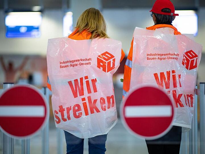 Zwei Mitarbeiterinnen von Reinigungsfirmen stehen mit Streikwesten am Flughafen Münster Osnabrück. Foto: Guido Kirchner/dpa