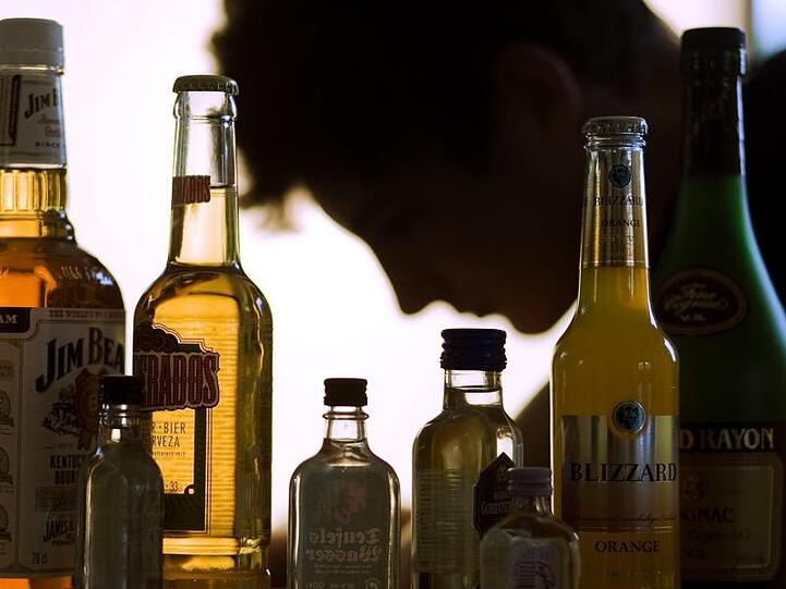 Ein Mann sitzt hinter Flaschen mit Alkohol. Foto: Jens Büttner/Archivbild