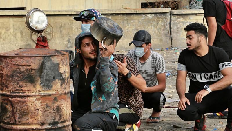Demonstranten hocken in Bagdad hinter Fässern und benutzen Töpfe und Pfannen als Kopfschutz, während Sicherheitskräfte den Zugang zur Grünen Zone blockieren. Demonstranten hocken in Bagdad hinter Fässern und benutzen Töpfe und Pfannen als Kopfschutz, während Sicherheitskräfte den Zugang zur Grünen Zone blockieren.