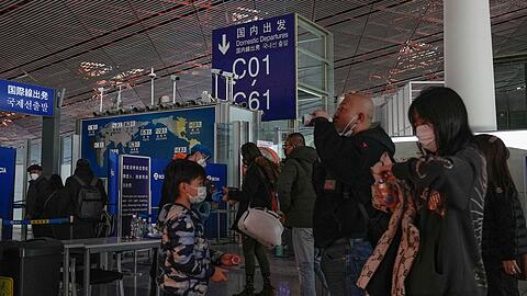Passagiere mit Mund-Nasen-Schutz stehen am Flughafen Peking an der Sicherheitskontrolle vor einem internationalen Abfluggate an.
