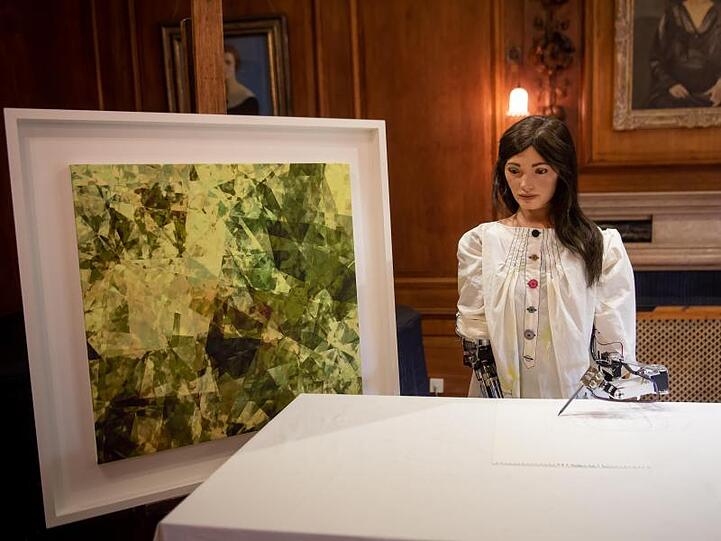 Ai-Da, die weltweit erste Roboterkünstlerin, in Oxford neben einem eigenen Kunstwerk.