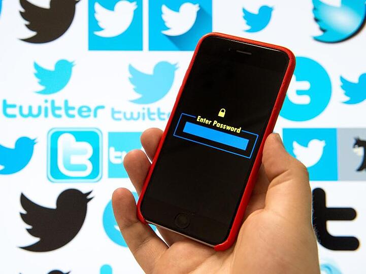 Logos vom Kurznachrichtendienst Twitter sind auf einem Bildschirm zu sehen, davor wird ein Handy mit einer Passwortmaske gehalten. Foto: Lino Mirgeler/Archiv