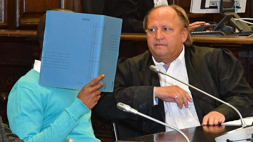 Hamburg: Der Angeklagte aus dem westafrikanischen Niger sitzt im Gerichtssaal neben seinem Anwalt Tim Burkert (r) und verbirgt sein Gesicht mit einem Aktendeckel.
