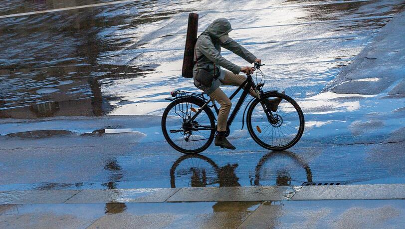 Eine Frau fährt bei Regen mit ihrem Rad durch die Münchner Innenstadt.