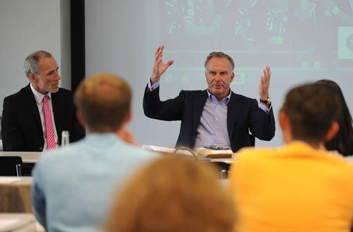 Karl-Heinz Rummenigge spricht zu Studierenden der Bayerischen Akademie für Werbung und Marketing (BAW) in München. Links neben ihm sitzt der Sportjournalist und Studienleiter der BAW, Peter Ehm.