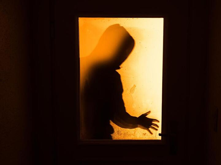 Der Schatten eines Mannes hinter einer gläsernen Wohnungstür.