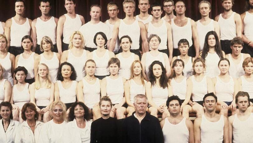 Einar Schleef mit Elfriede Jelinek inmitten des Chor-Ensembles von Jelineks „Ein Sportstück“, das Schleef 1998 am Wiener Burgtheater zur Uraufführung brachte. Sport wurde hier als eine andere Form von Krieg, als Massenphänomen und letzter Rückzugsort der Uniform erzählt. Einar Schleef mit Elfriede Jelinek inmitten des Chor-Ensembles von Jelineks „Ein Sportstück“, das Schleef 1998 am Wiener Burgtheater zur Uraufführung brachte. Sport wurde hier als eine andere Form von Krieg, als Massenphänomen und letzter Rückzugsort der Uniform erzählt.