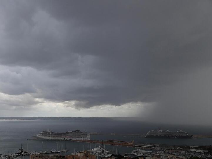 Dunkle Regenwolken hängen über der Bucht und dem Hafen, in dem zwei Kreuzfahrtschiffe liegen.