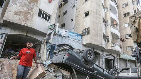 Ein Mann geht an einem umgestürtzen Autowrack vor einem Wohnhaus, welches zuvor von israelischen Luftangriffen getroffen wurde, vorbei.