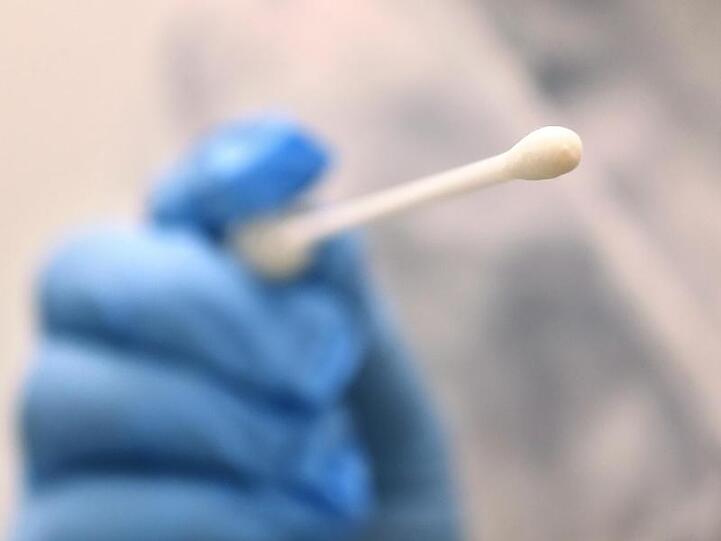 Ein Arzt hält in einer Hausarztpraxis einen Tupfer für einen Coronatest-Abstrich.