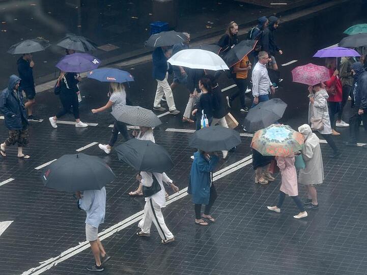 Fußgänger schützen sich mit Regenschirmen vor starkem Regen. Der Niederschlag bringt angesichts der anhaltenden Buschbrände in New South Wales etwas Entlastung für die Einsatzkräfte.