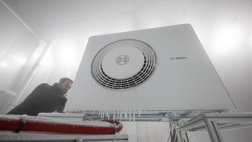 Ein Mitarbeiter der Bosch Thermotechnik GmbH öffnet in einer Klimakammer das Gehäuse einer Bosch-Wärmepumpe.