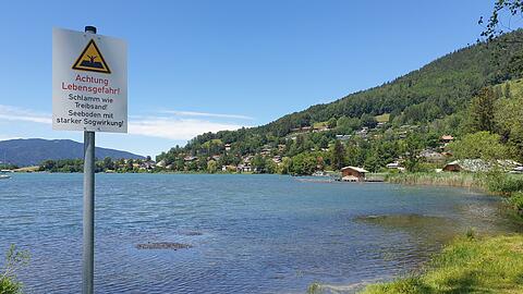 An der Schwaighofbucht in Tegernsee-Süd warnt ein Schild vor dem "Schlamm wie Treibsand". Seit Jahren wird über die Entsorgung des Schlamms gestritten. Nun gibt es auch am Chiemsee Konflikte über die Ausbaggerung.