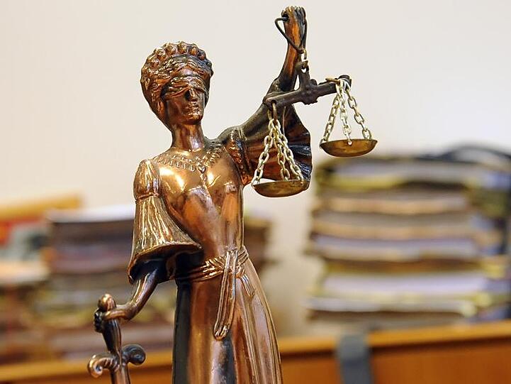 Eine goldfarbene Justitia-Figur steht vor Aktenbergen. Foto: Britta Pedersen/Archiv