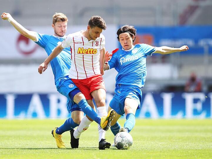 Alexander Mühling (l) und Lee Jae-Sung von Holstein Kiel bedrängen Charalampos Makridis von Regensburg. Foto: Alexander Hassenstein/Getty Images Europe/Pool/dpa