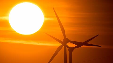 Die Sonne geht hinter Windrädern auf.