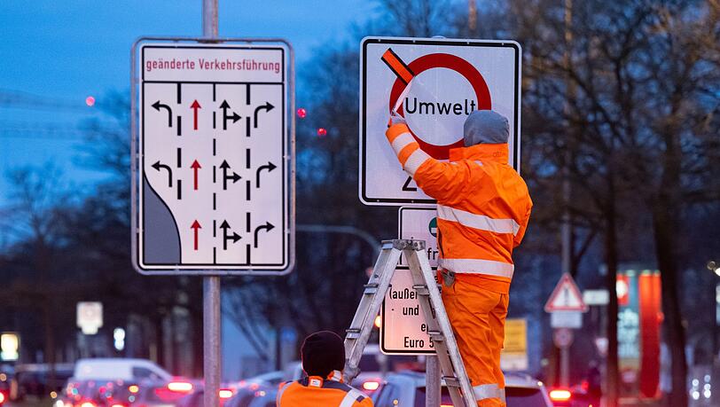 Arbeiter entfernen einen roten Klebestreifen von einem Schild.