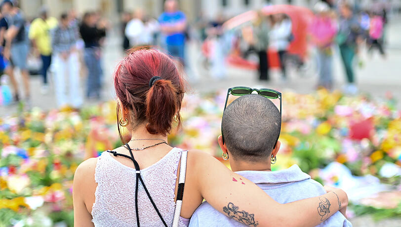 Menschen schauen sich Beileidsbekundungen, Blumen, Flaggen und Kerzen an, die vor dem Brandenburger Tor abgelegt wurden.