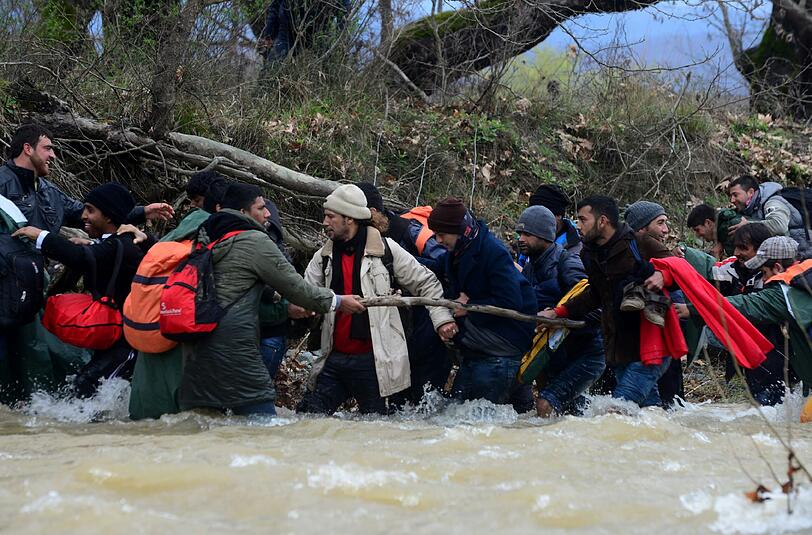 Migranten und freiwillige Helfer bilden eine Menschenkette im Fluss.