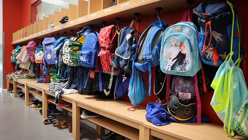 Sporttaschen und Schulranzen hängen an der Garderobe vor einem Klassenzimmer.