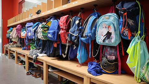 Sporttaschen und Schulranzen hängen an der Garderobe vor einem Klassenzimmer.