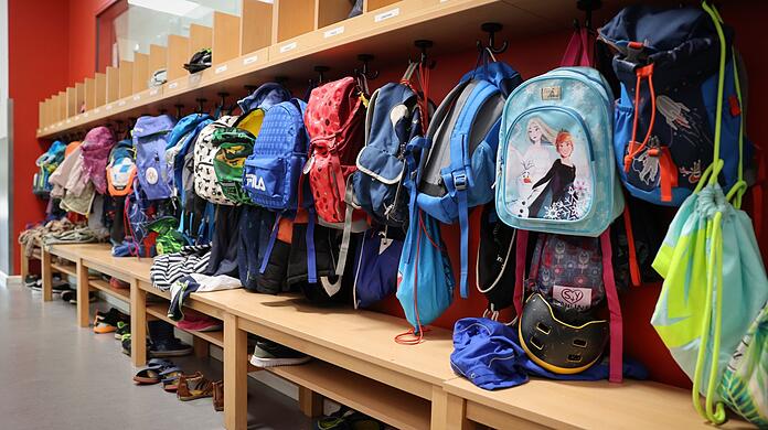 Sporttaschen und Schulranzen hängen an der Garderobe vor einem Klassenzimmer.
