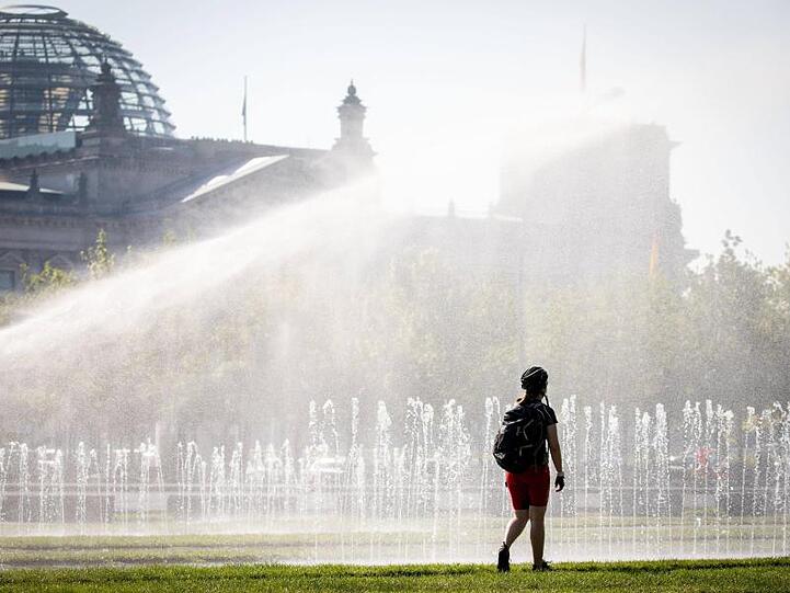 Eine Passantin erfrischt sich in einer Wasserfontäne vor dem Reichstag in Berlin. Nicht nur die Hauptstadt schwitzt.
